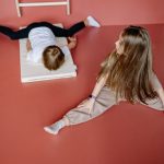 Two children engaging in gymnastics on a mat indoors, showcasing flexibility and playfulness.