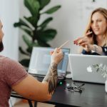 Man and woman discussing work at a table with laptops in a modern office.
